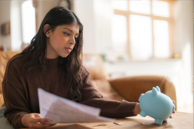 young female victim of predatory lending reading bills and staring sadly at empty piggy bank